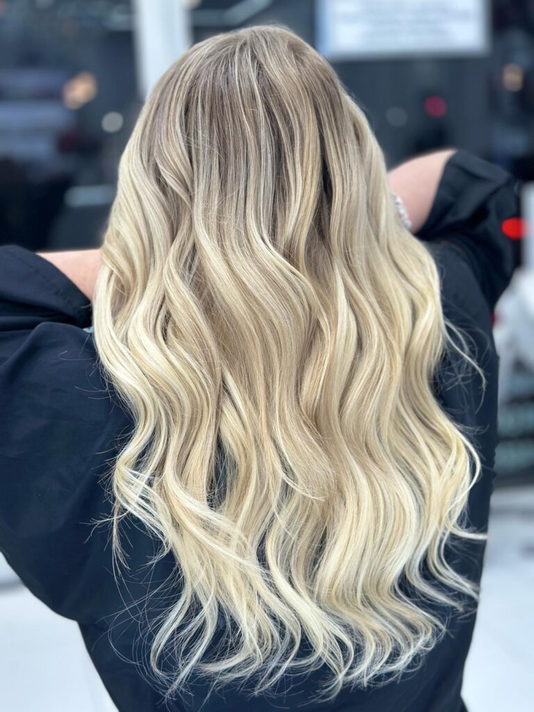 Long blonde balayage hair styled in loose waves, viewed from behind
